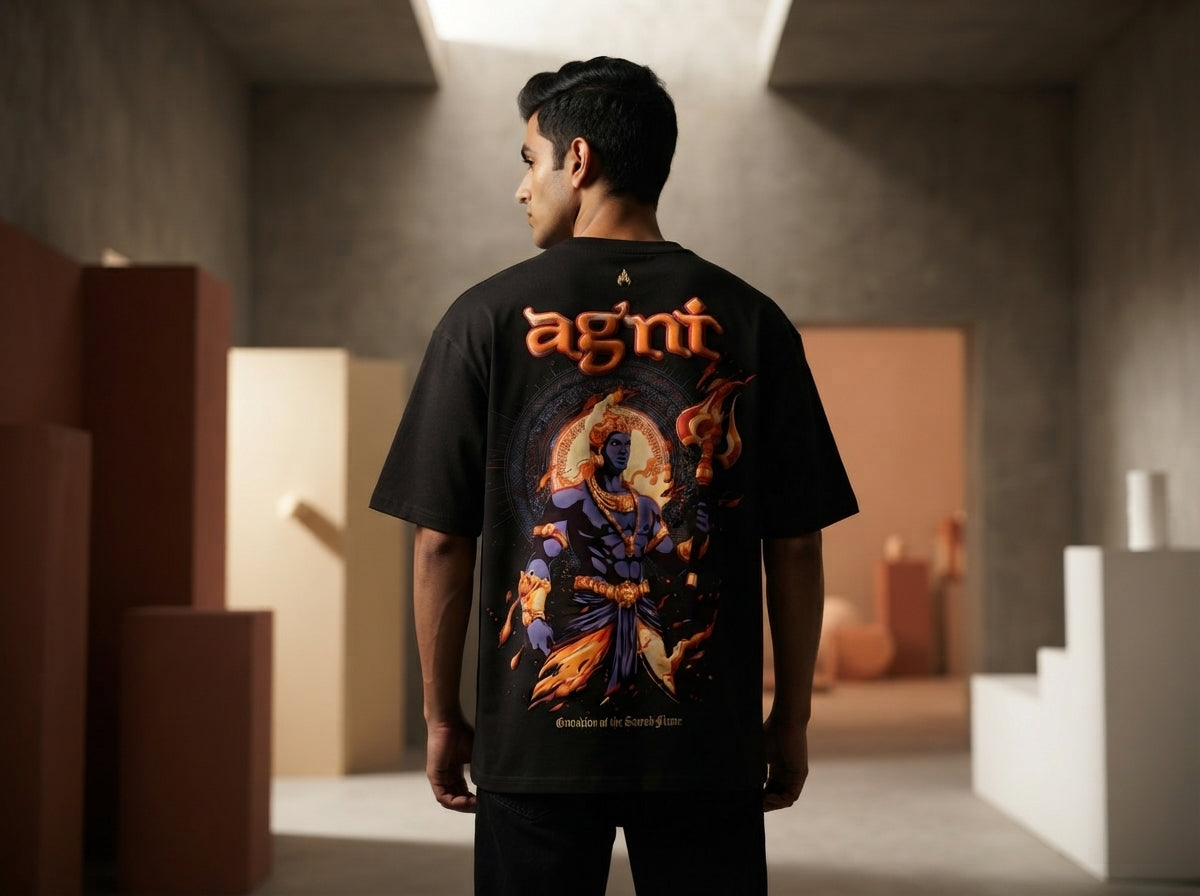 A young South Asian man wearing an Agni oversized puff print T-shirt in a modern, warmly lit minimalist room.