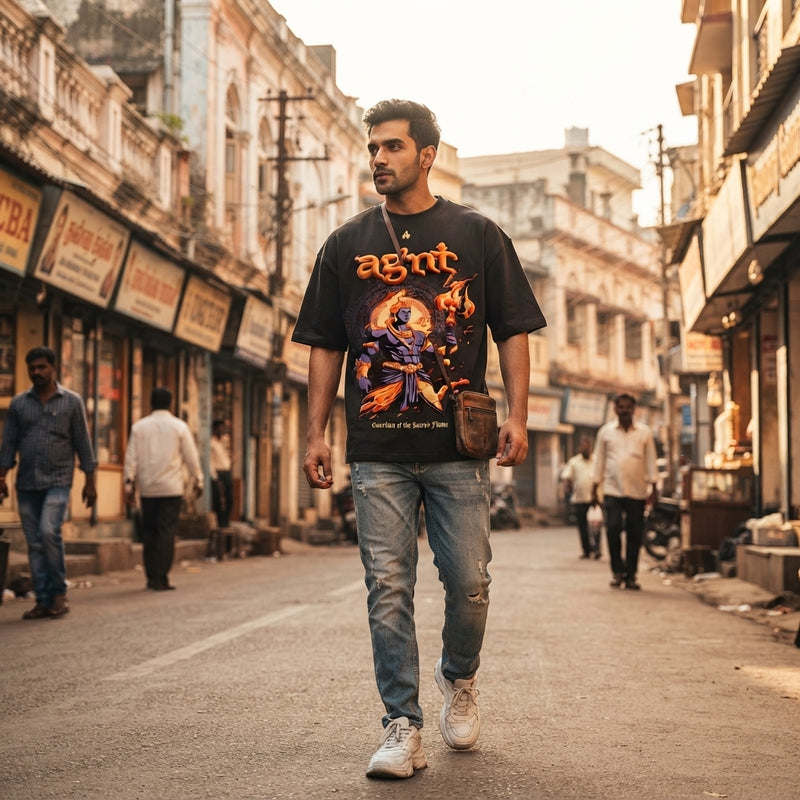 A South Asian man wearing a graphic oversized T-shirt walking down a sunny Bangalore street.